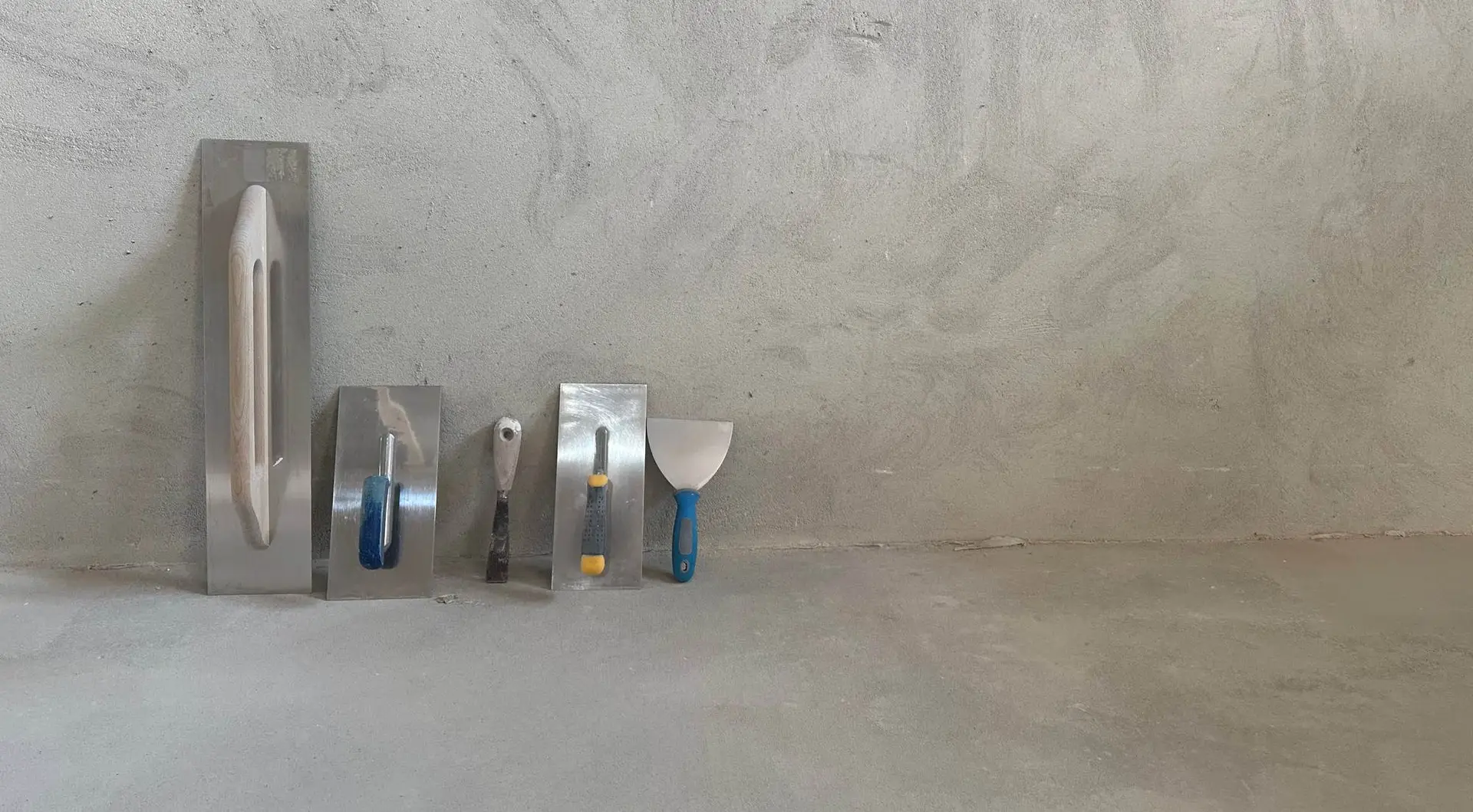 Truelles et couteaux à enduire posés devant un mur en béton ciré gris