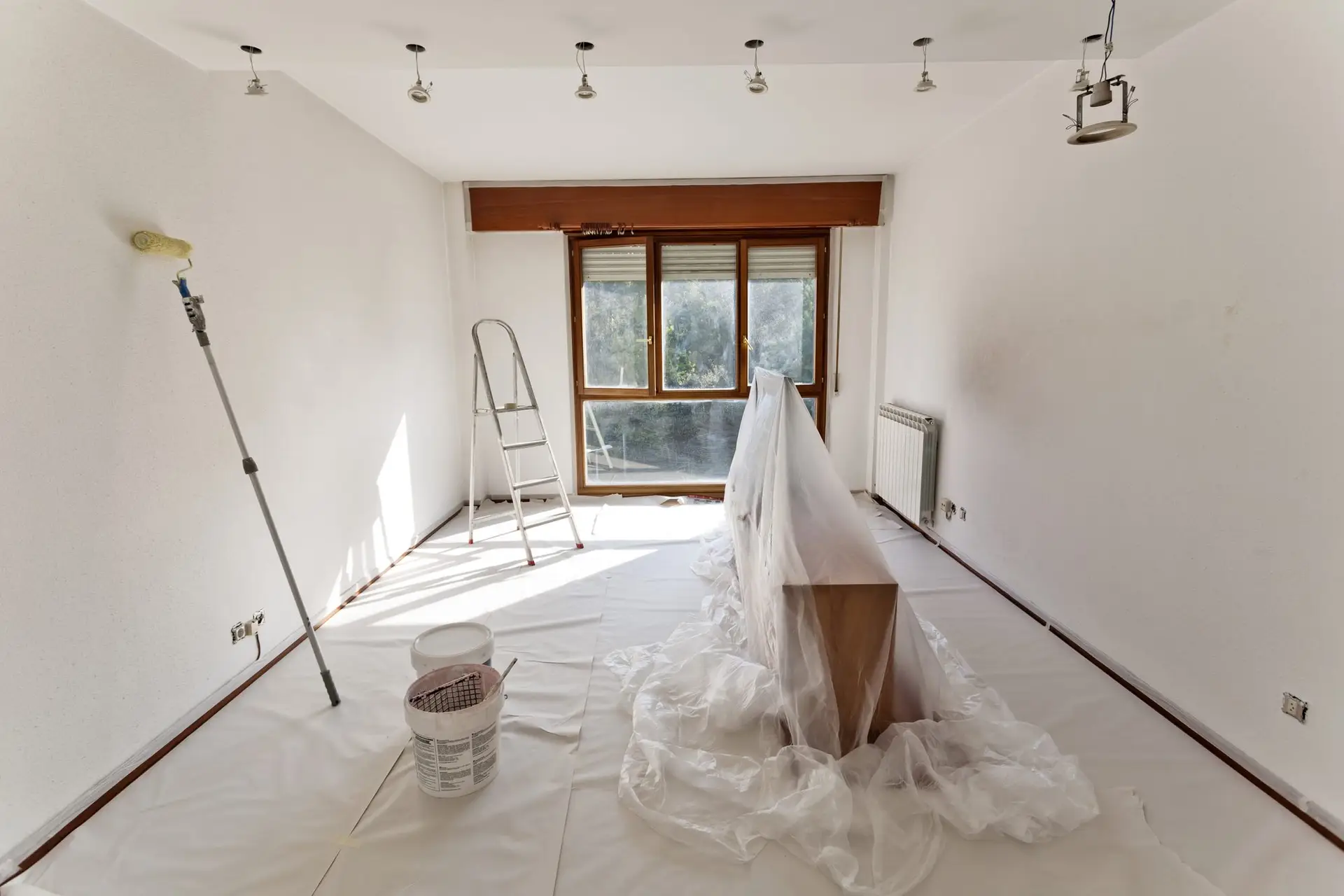 Chambre vidée avant peinture, meubles bâchés, escabeau et pots au sol