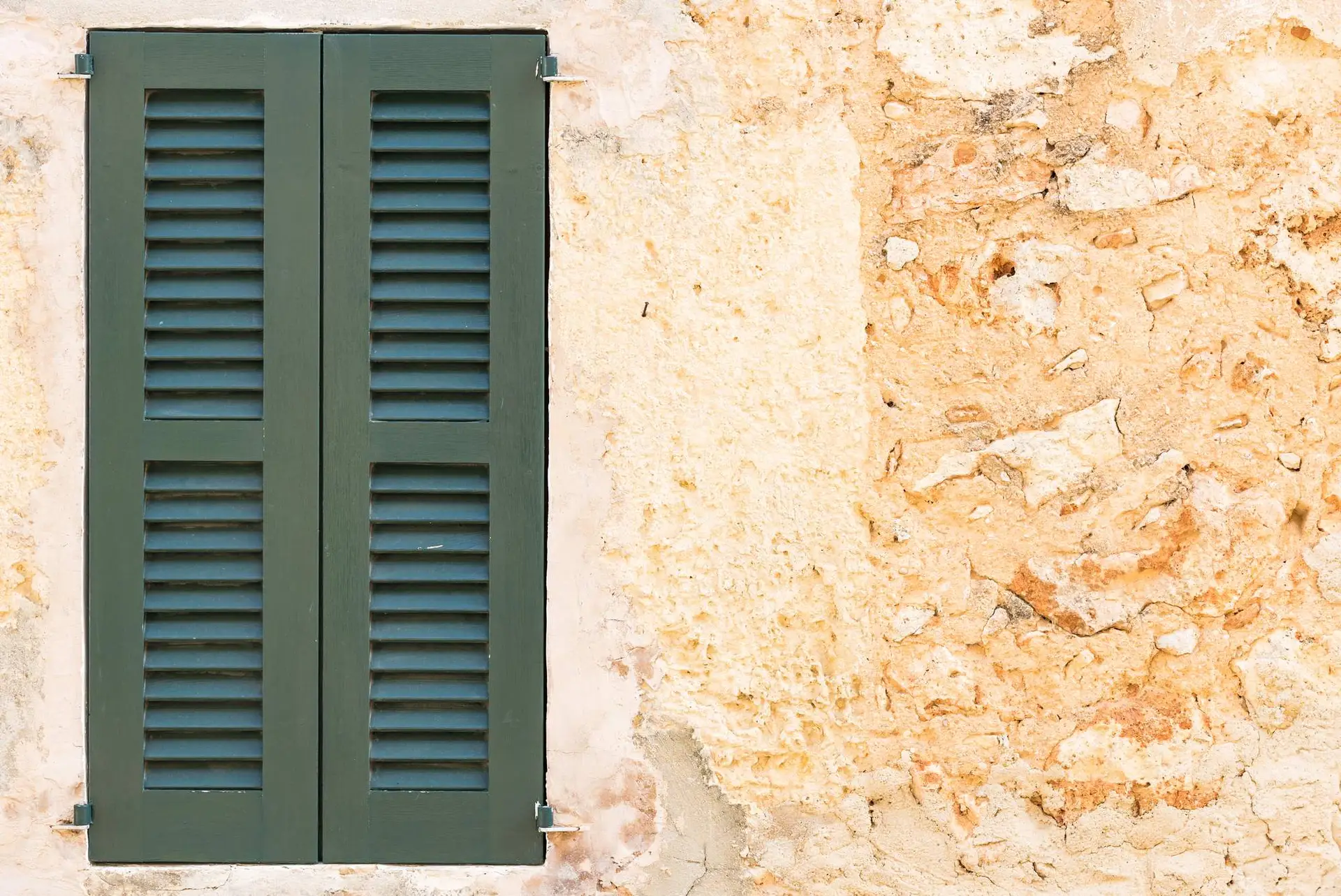 Volets verts fermés sur une façade ancienne à l’enduit ocre écaillé